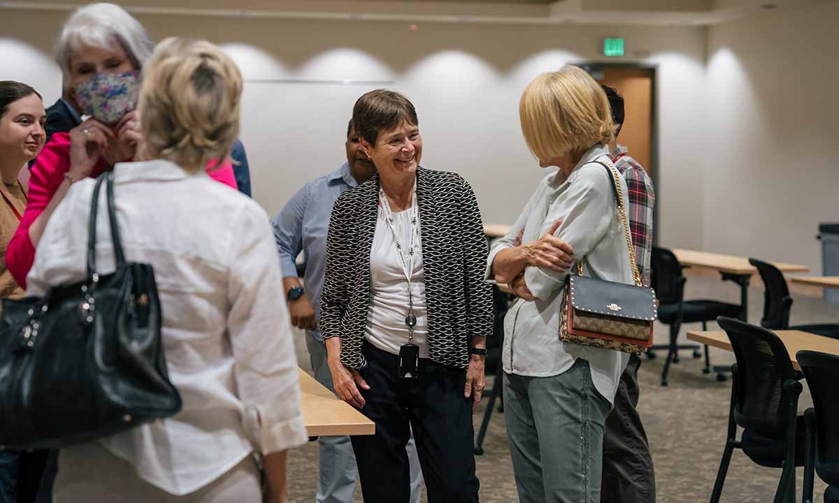 Sherrie L. Perkins stands in the center of a group of people chatting and smiling in a conference room.